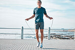 Jump rope, happy and man workout by the beach for his outdoor morning exercise, training and fitness routine. Athlete, cardio and male skipping by the ocean or sea for wellness lifestyle