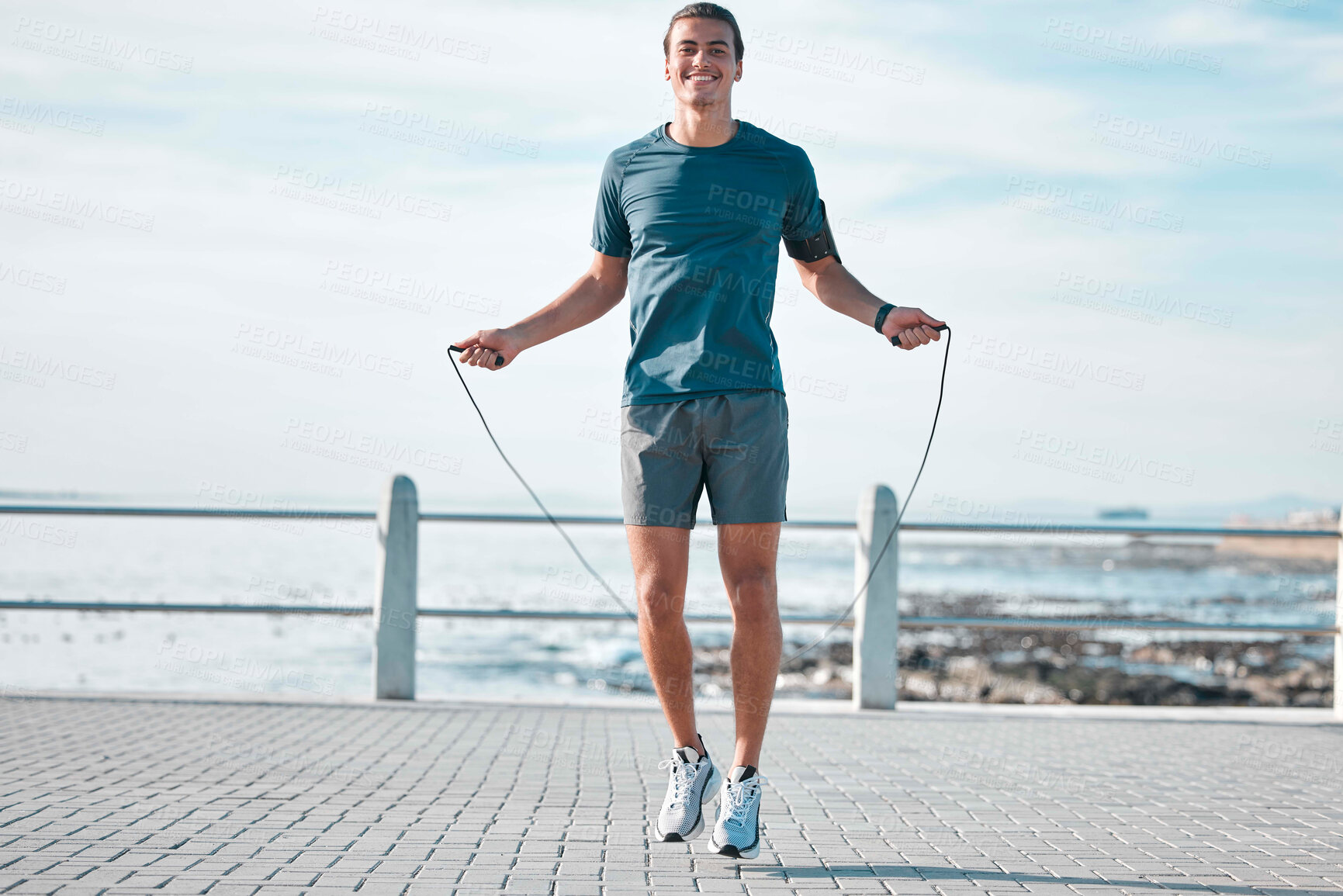 Buy stock photo Jump rope, happy and man workout by the beach for his outdoor morning exercise, training and fitness routine. Athlete, cardio and male skipping by the ocean or sea for wellness lifestyle