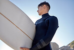 Surfing, beach and man with blue sky outdoor for water sports, training and exercise. Surfboard, morning workout and sea with summer sun and young surfer ready for sport and freedom at the ocean