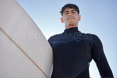 Surfing, beach and serious surfer with blue sky outdoor for water sports, training and exercise. Surfboard, morning workout and sea with summer sun and man ready for sport and freedom at the ocean
