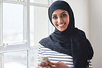 Portrait muslim woman smiling using smartphone wearing hijab headscarf standing by window