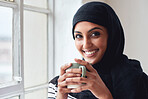 Portrait happy muslim woman smiling by window holding coffee wearing hijab headscarf