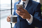 Businessman hands using smartphone holding coffee texting on mobile phone in office standing by window
