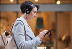 Young business woman using smartphone listening to music wearing headphones texting on mobile phone in city