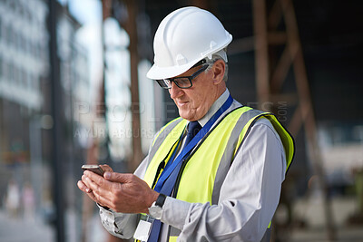 Mature construction worker man using smartphone browsing messages on site wearing hard hat and reflective vest in city