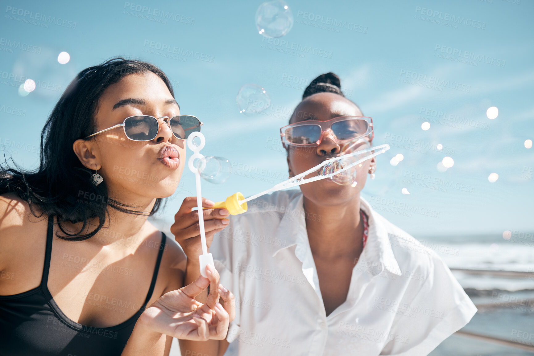 Buy stock photo Friends, playing or blowing bubbles by beach, ocean or sea in summer holiday, travel vacation or bonding activity. Women, people or students and soap wand or toy in fun game, freedom or social break 