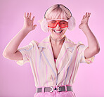 Fashion, beauty and happy woman isolated on pink background with excited, wow and dancing in pink aesthetic. Earmuffs, clothes and cool, retro and punk sunglasses of gen z model or person in studio