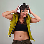 Music, dance and woman with headphones in studio, happy and excited isolated on grey background. Streaming service, song and gen z fashion, girl dancing with hands up and smile to online radio dj.