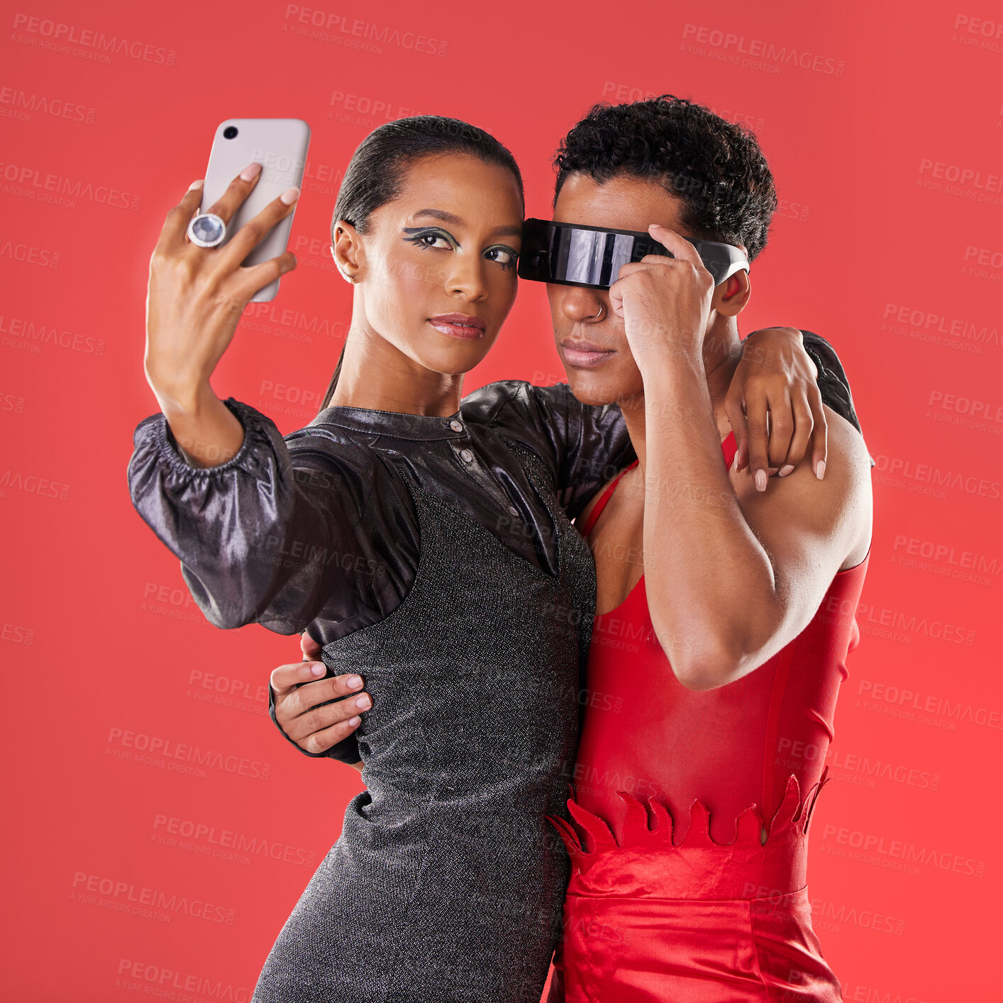 Buy stock photo Selfie, fashion and funky people isolated on red background for queer, creative gen z and cyberpunk aesthetic. Futuristic glasses, profile picture and beauty couple of friends, model or youth makeup