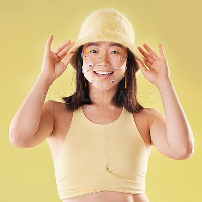 Buy stock photo Fashion, asian and portrait of a woman with comic eyes isolated on a yellow background in studio. Happy, funny and face of a girl model with a hat and smile for advertising, cosmetics and motivation