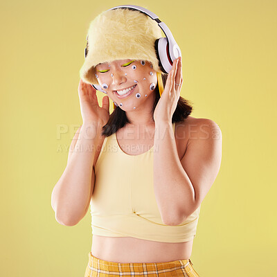 Buy stock photo Music headphones, makeup and woman in studio isolated on a yellow background. Eye stickers, freedom technology and happy female model listening, enjoying and streaming radio, podcast and audio song.