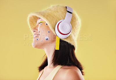Buy stock photo Makeup, music headphones and woman in studio isolated on a yellow background. Eye stickers, technology and smile of happy female model listening, enjoying and streaming radio, podcast and audio song.