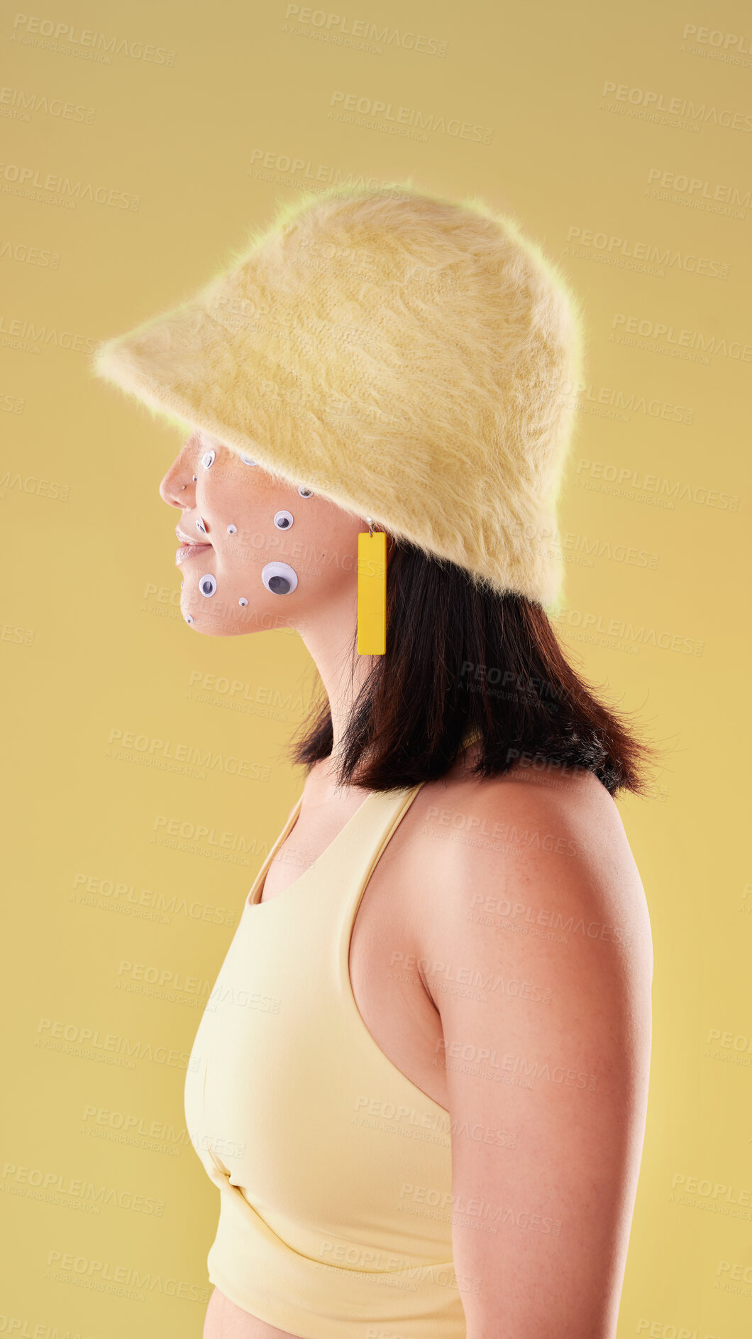 Buy stock photo Yellow fashion, eye sticker and woman on studio background for cosmetics, style and makeup. Beauty, creative aesthetic and profile of gen z girl with eyes on face for emoji, art and trendy clothes