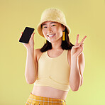 Portrait, peace sign and Asian woman with phone in studio isolated on a yellow background mockup. Makeup, fashion and smile of happy female with v hand gesture and mobile smartphone for advertising.