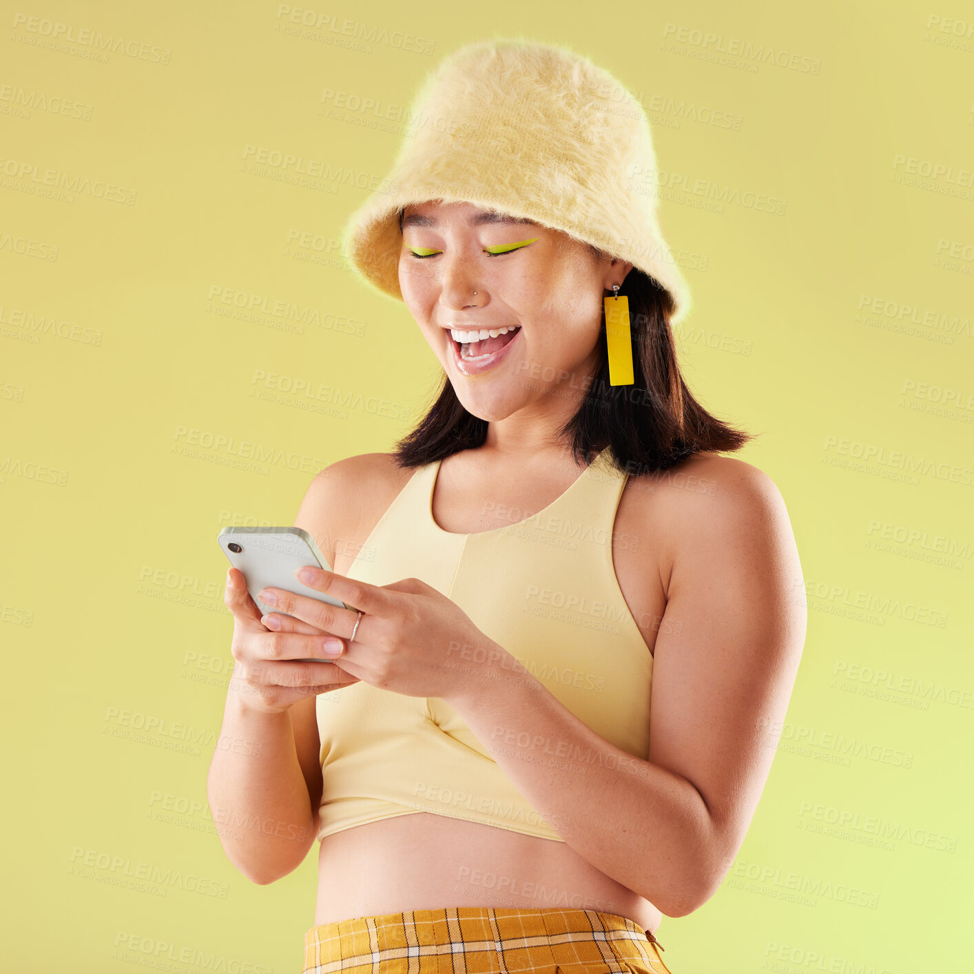 Buy stock photo Phone, laughing and Asian woman typing in studio isolated on a yellow background. Comic emoji, technology and happy female model laugh at funny meme with mobile smartphone for social media or texting