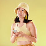 Phone, thinking and Asian woman typing in studio isolated on a yellow background. Ideas, technology and female model contemplating, focus or lost in thoughts with mobile for social media and texting.