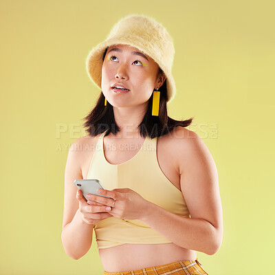 Buy stock photo Phone, thinking and Asian woman typing in studio isolated on a yellow background. Ideas, technology or female model contemplating, decision or lost in thoughts with mobile for social media or texting