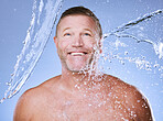 Showering, water splash and man with smile, cleaning and daily hygiene on blue studio background. Mature male, gentleman and clear liquid for washing, dermatology and skincare for grooming on backdrop