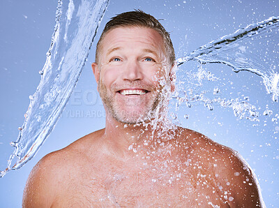 Buy stock photo Showering, water splash and man with smile, cleaning and daily hygiene on blue studio background. Mature male, gentleman and clear liquid for washing, dermatology and skincare for grooming on backdrop