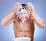 Man, water splash and face wash by basin for hygiene or natural sustainability against a blue studio background. Male washing by sink for clean wellness, skincare or self care for facial treatment