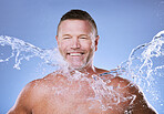 Water splash, face and mature man in studio for cleaning, hygiene and wellness on a blue background. Skincare, facial and body care for aging skin of male model in luxury, pamper or beauty routine