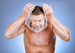 Man, face and water splash in skincare hygiene for natural sustainability against a blue studio background. Male washing for clean health and wellness in self love or care for facial treatment