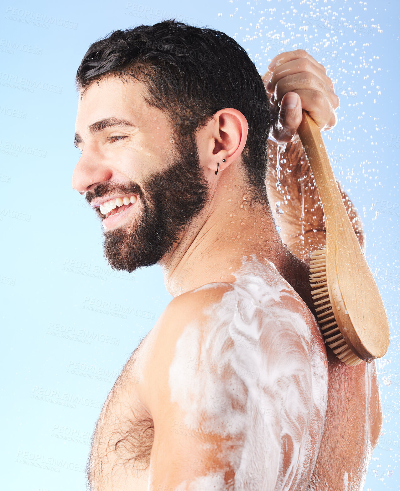 Buy stock photo Shower, cleaning and man with brush, water splash and soap in studio for wellness, hygiene and grooming. Skincare, self care and male with foam, bath cosmetics and washing body on blue background