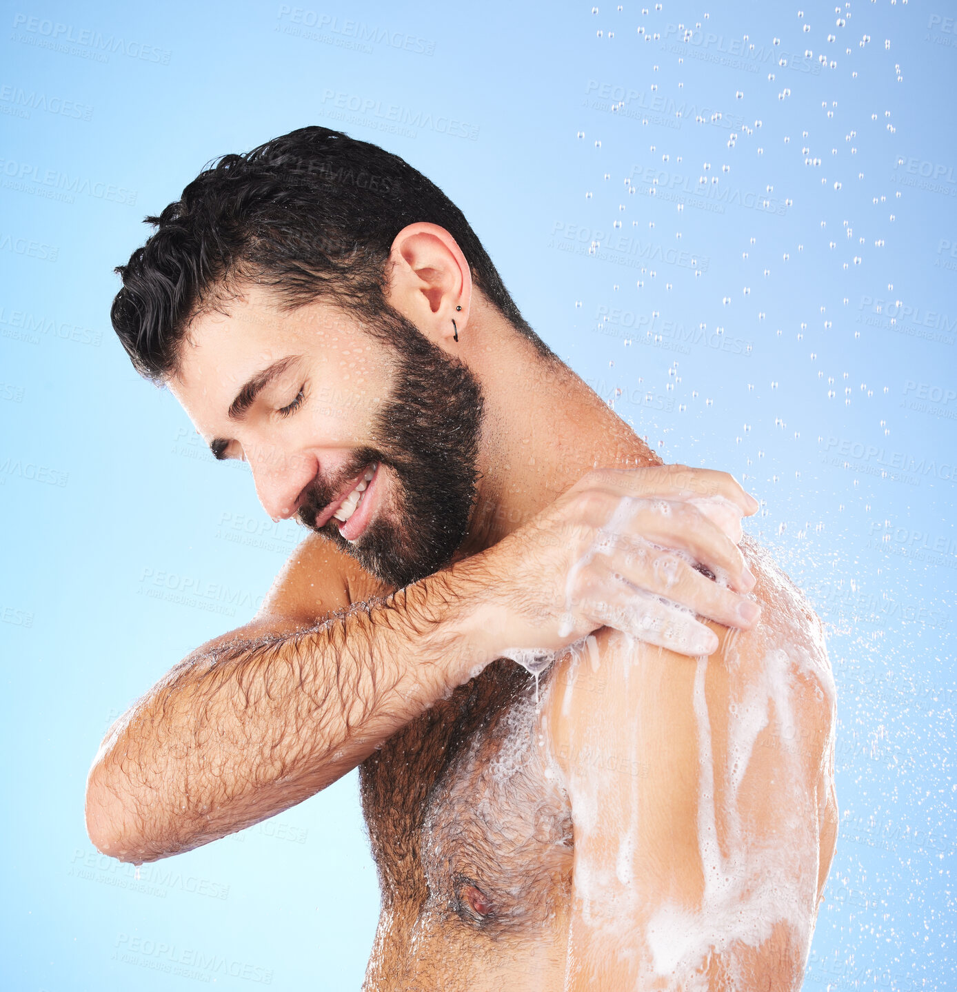 Buy stock photo Shower, cleaning and man with water, smile and soap in studio for wellness, hygiene and grooming. Skincare, healthy skin and happy male with foam, bath cosmetics and washing body on blue background