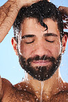 Washing, hair and man in studio for skincare, grooming and hygiene against blue background. Haircare, body care and guy model relax in shower, happy and isolated on water splash, cosmetic or wellness