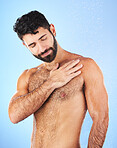 Shower, body care and man in studio for wellness, hygiene and skincare against blue background. Cleaning, chest and male model relax in luxury, water splash and beauty routine isolated in a bathroom 