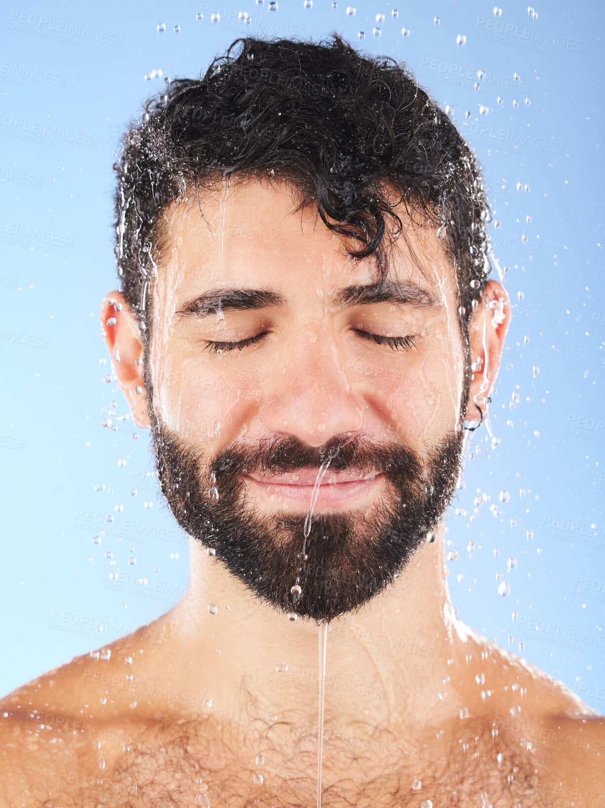 Buy stock photo Man, water drop and face for hygiene, self care and cleaning on blue background in studio. Aesthetic model person for skincare, health and wellness with shower splash for facial dermatology cosmetics