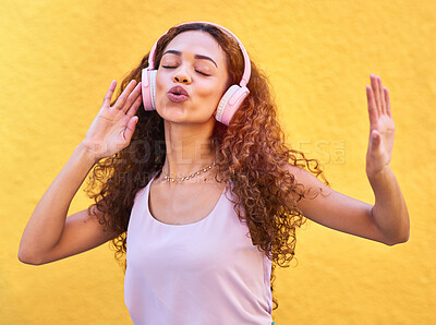 Buy stock photo Music, freedom and singing with a black woman listening to the radio outdoor on a yellow wall background. Headphones, energy and face with an attractive young female streaming audio sound for fun