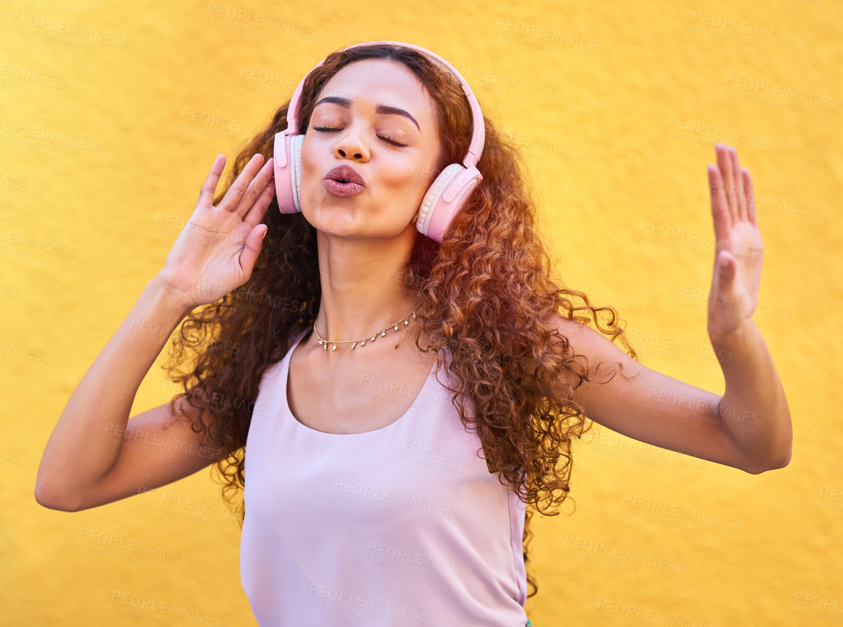 Buy stock photo Music, freedom and singing with a black woman listening to the radio outdoor on a yellow wall background. Headphones, energy and face with an attractive young female streaming audio sound for fun