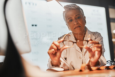 Buy stock photo Glasses, optometry and check with a mature woman optician looking at a pair of frame spectacles in the office. Eyewear, healthcare and examine with a female optometrist checking prescription lenses