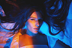 Portrait, vaporwave lights and young woman face in bedroom with creative disco lighting. Makeup, beauty and model resting and feeling relax and calm on a bed pillow with cyberpunk aesthetic 