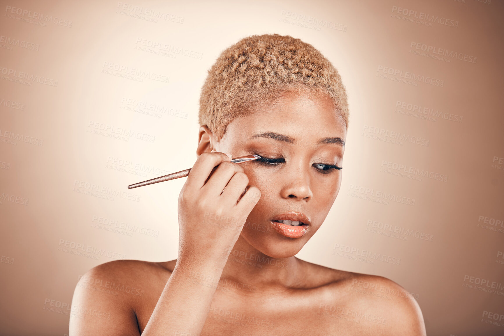 Buy stock photo Black woman, beauty and brush for eye makeup on a brown background with cosmetics for face. Aesthetic model person in studio for transformation, self care and facial glow or shine on skin and eyes