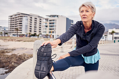 Buy stock photo Woman, serious and stretching legs outdoor at beach sidewalk for energy, wellness and healthy mindset. Senior lady, exercise and warm up body at sea promenade for sports, thinking and running workout