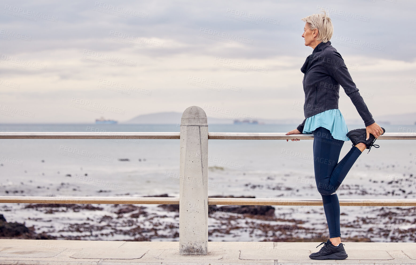 Buy stock photo Senior woman, fitness and stretching at beach promenade for exercise, wellness and thinking on sky mockup. Lady, runner and person warm up legs at sea, healthy workout and running mindset at ocean