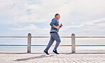 Senior man running outdoor at beach promenade, sky mockup and energy for body, wellness and cardio workout. Elderly male, exercise and runner at seaside for sports training, fitness or healthy action