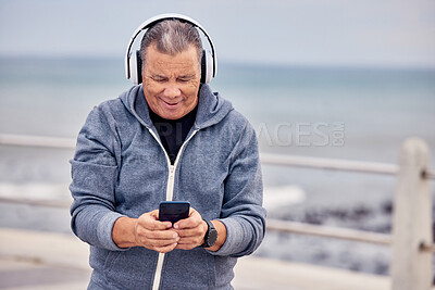 Buy stock photo Music, phone and senior man by ocean for fitness, exercise and training for healthy lifestyle on promenade. Retirement, headphones and elderly male listening to audio, track or radio and texting