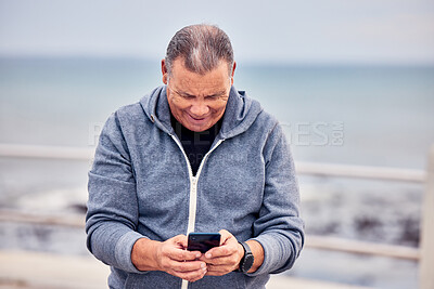 Buy stock photo Senior man, phone and typing outdoor for exercise at beach promenade, social media and internet search on tech. Elderly male, sports and smartphone at ocean for mobile app, digital health and fitness