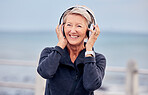 Old woman at beach, headphones and listen to music with smile on face, happiness and freedom outdoor. Fitness, fresh air and technology, podcast or radio streaming with mature female in retirement