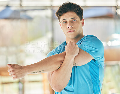 Portrait, fitness and man stretching arm in gym for health, wellness and flexibility. Sports face, training and male athlete stretch, warm up and getting ready to start workout, exercise or running.