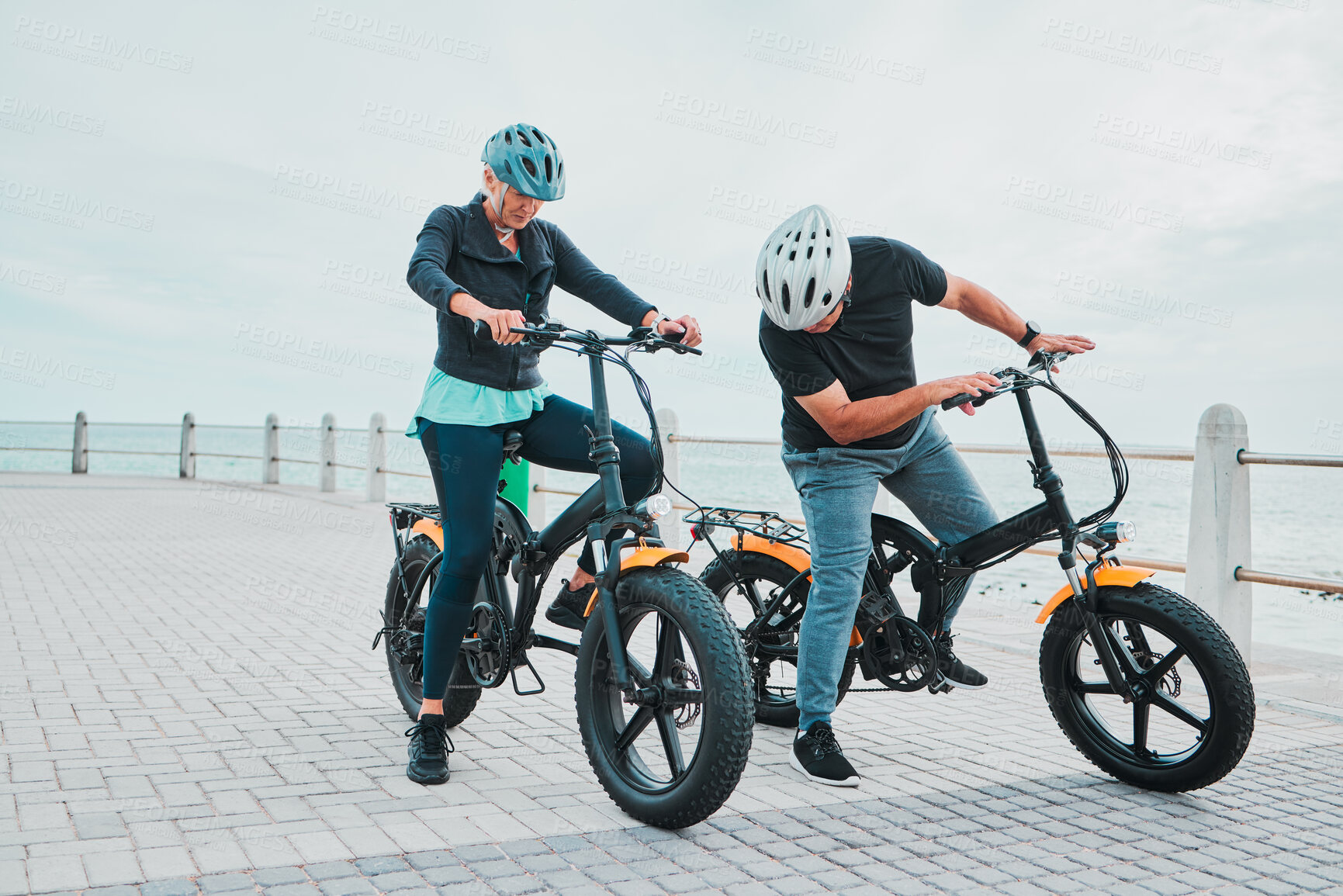 Buy stock photo Mature couple, electrical or checking bike by beach in bonding transportation, clean energy or sustainability city travel. Ebike, electricity or eco friendly bicycle for elderly man or cycling woman