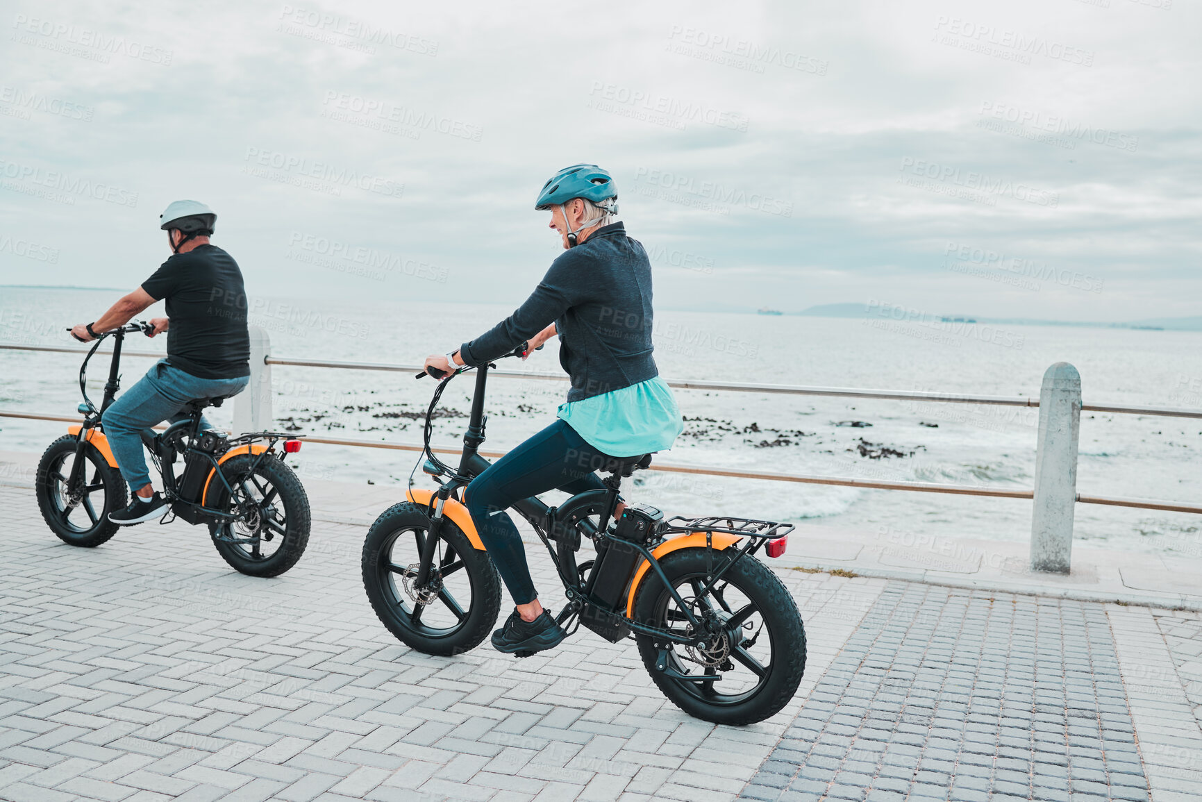 Buy stock photo Couple, helmet or electrical bike by sea or ocean beach in bonding transport, clean energy or sustainability travel. Technology, electric or eco friendly bicycle for happy woman or mature cycling man