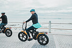 Couple, helmet or electrical bike by beach, ocean or sea in future transport, clean energy or sustainability travel. Technology, electric or eco friendly bicycle for happy woman or mature cycling man