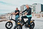 Senior couple, electric bike and smile by the beach for fun bonding cycling or travel together in the city. Happy elderly man and woman enjoying cruise on electrical bicycle for trip in Cape Town