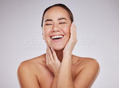 Buy stock photo Beauty, skincare and face of a woman in studio happy about dermatology cosmetic for glow. Aesthetic asian model person with hands on skin laughing about makeup and facial self care on grey background