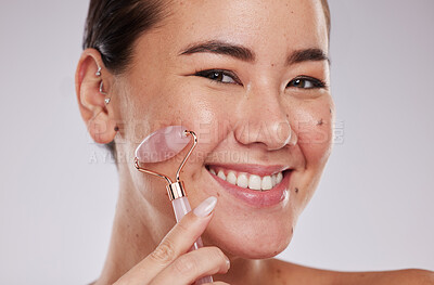 Buy stock photo Face skincare, portrait and Asian woman with roller in studio isolated on gray background. Dermatology aesthetics, beauty and happy female model with rose quartz stone or crystal for skin health.