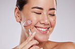 Face, eyes closed and skincare of Asian woman with jade roller in studio isolated on gray background. Dermatology aesthetics, beauty or happy female model with rose quartz stone or crystal for health